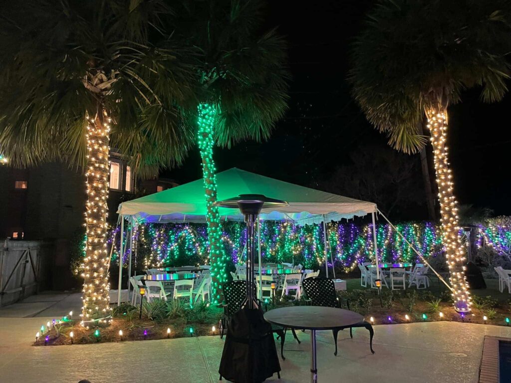Outdoor party tent and palm trees wrapped in colorful lights