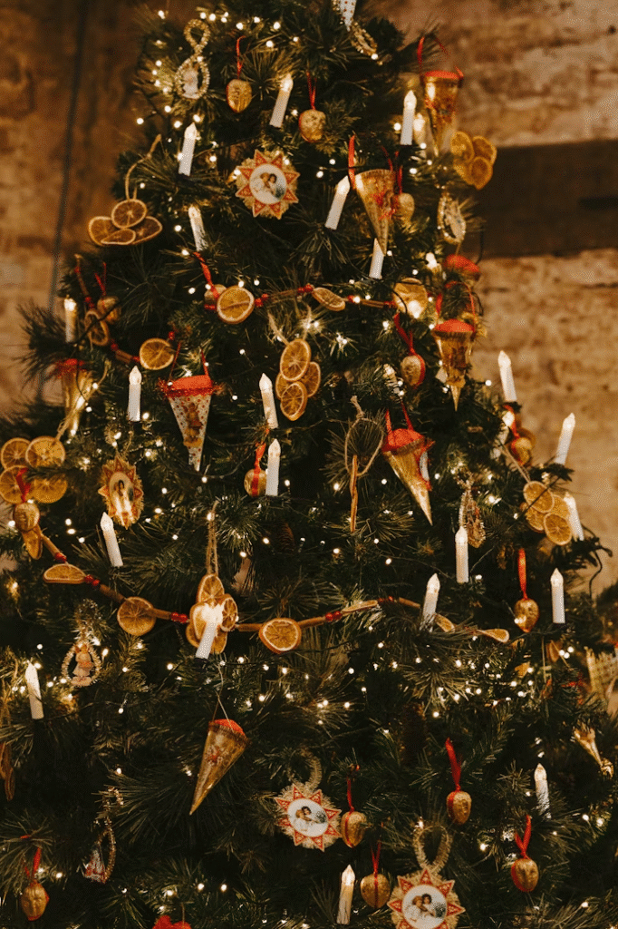 Traditional Christmas tree decorated with dried orange slices, small candles, and vintage-style ornaments, all illuminated by warm white string lights.