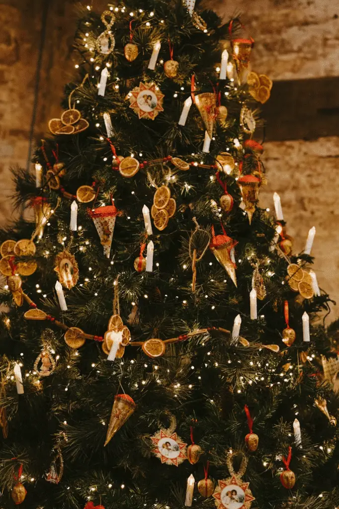 Traditional Christmas tree decorated with dried orange slices, small candles, and vintage-style ornaments, all illuminated by warm white string lights.