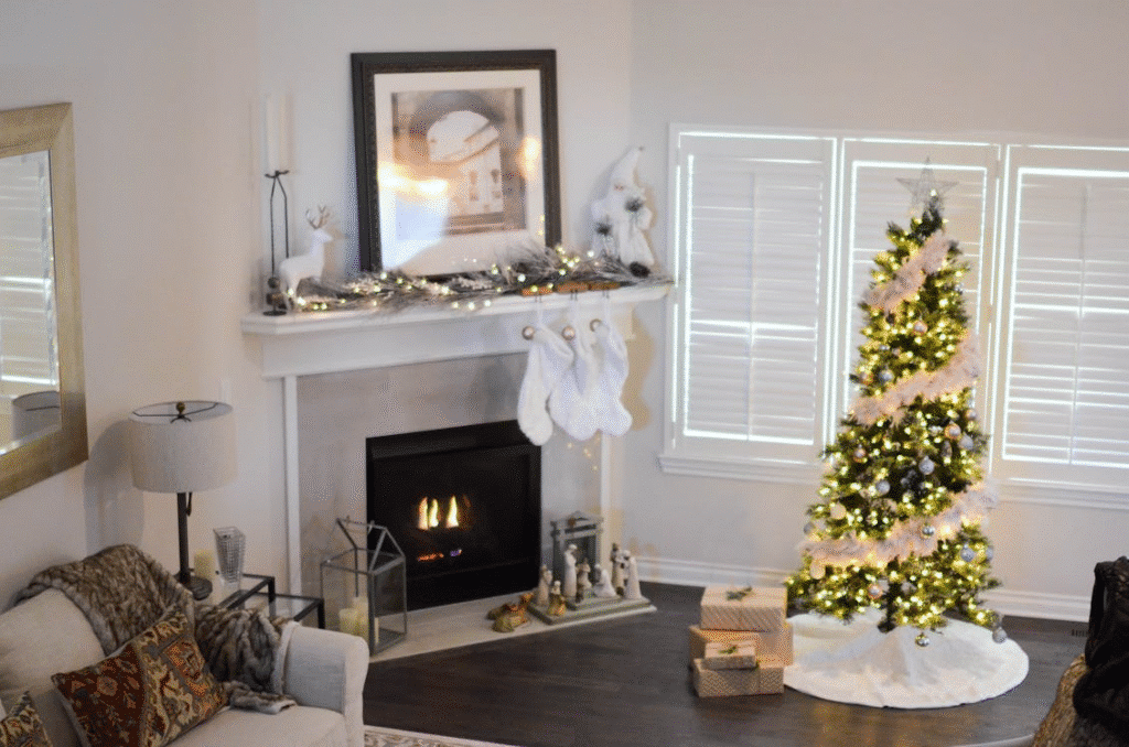 Cozy living room decorated for Christmas with a lit fireplace, white stockings hanging on the mantel, a glowing Christmas tree adorned with lights and garland, and wrapped presents underneath.